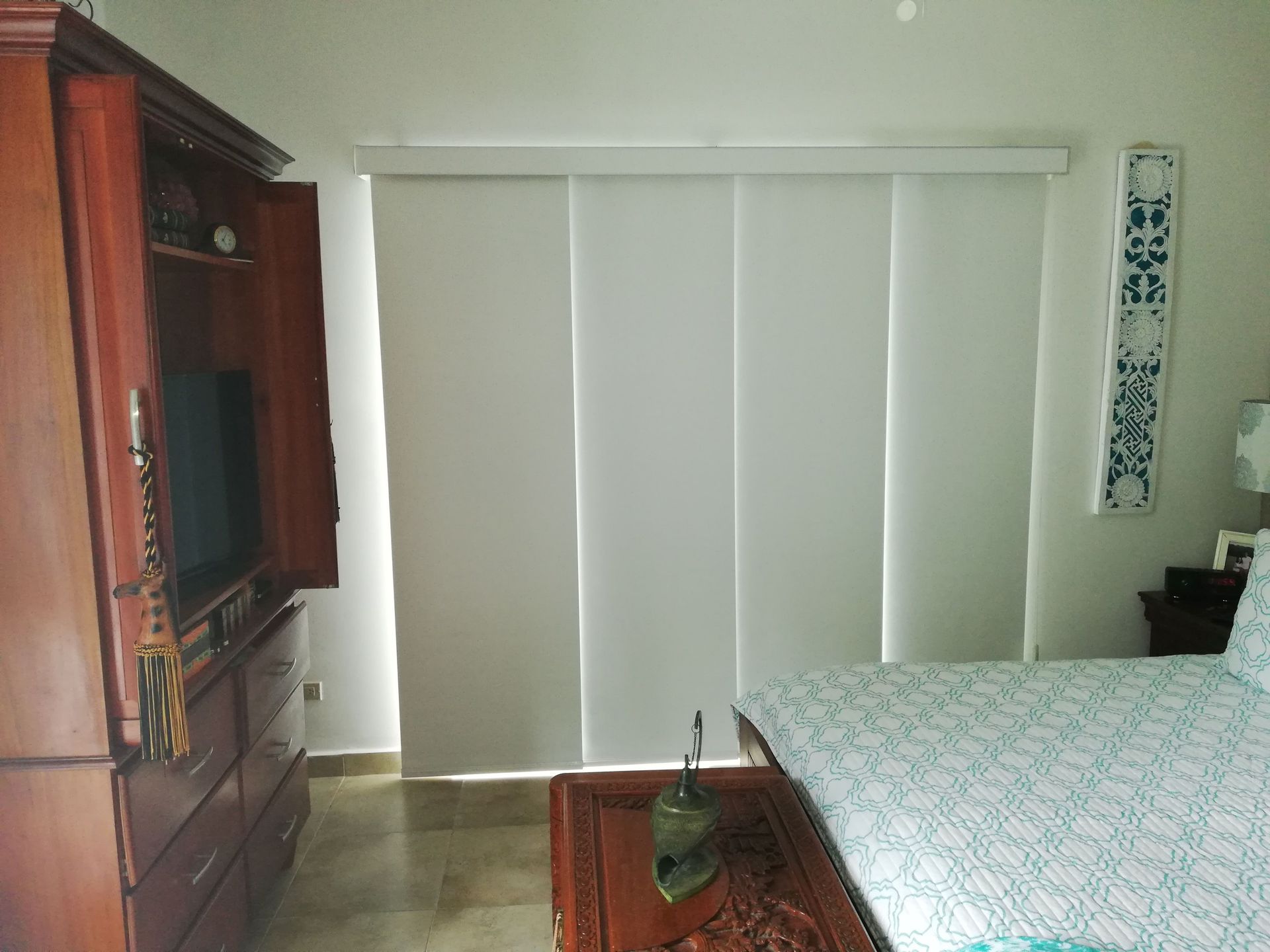 Dormitorio con gran mueble de madera, persianas corredizas blancas y cama con ropa de cama estampada.