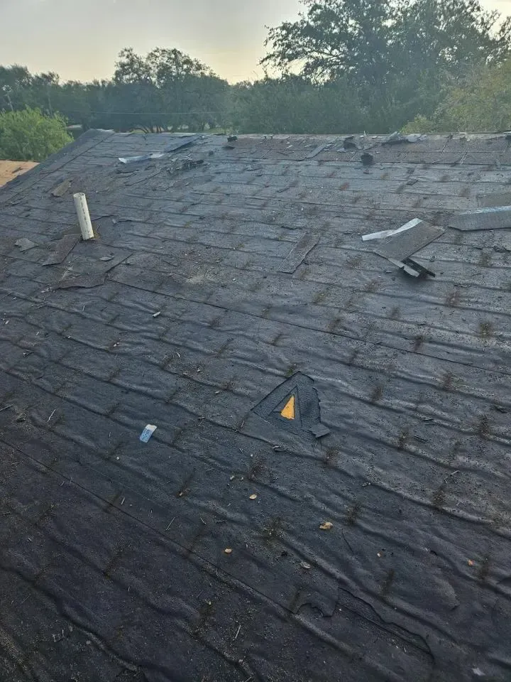 Damaged shingled roof with scattered debris and a small hole near the center at dawn
