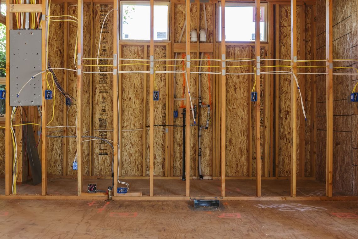 Framed interior wall under construction with exposed wood studs, insulation, and a small window.