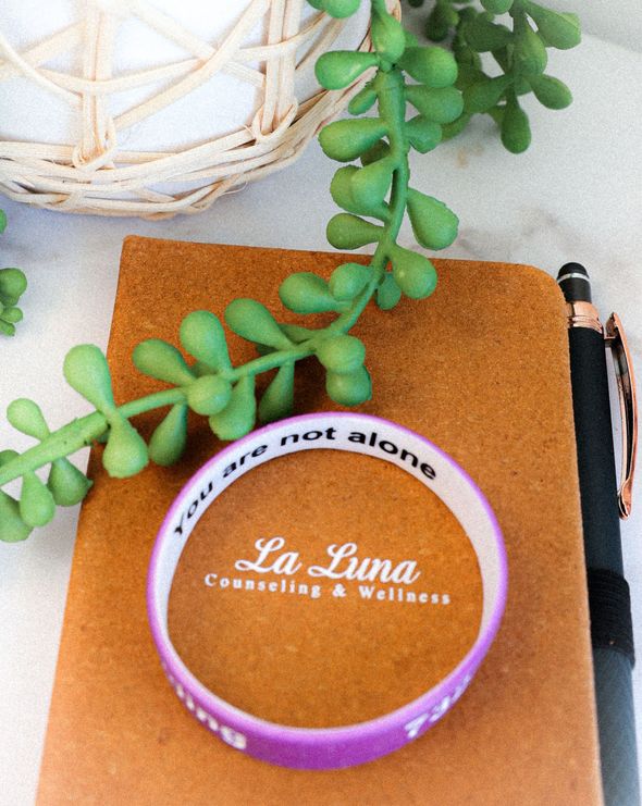 Purple “La Luna Counseling & Wellness” candle with succulent on a brown notebook and pen.