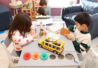Children playing at a table with toys and a yellow school bus in a playroom