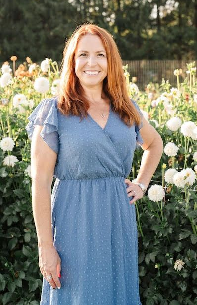Smiling woman in a blue dress standing in a flower garden with white blooms