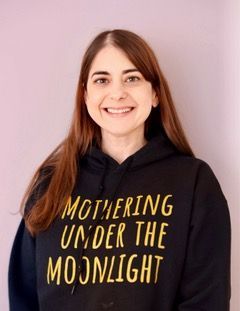 Smiling woman in a black hoodie with yellow text “MOTHERING UNDER THE MOONLIGHT” against a pink background