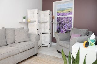 Bright living room with gray sofas, white screen divider, and a floral window painting