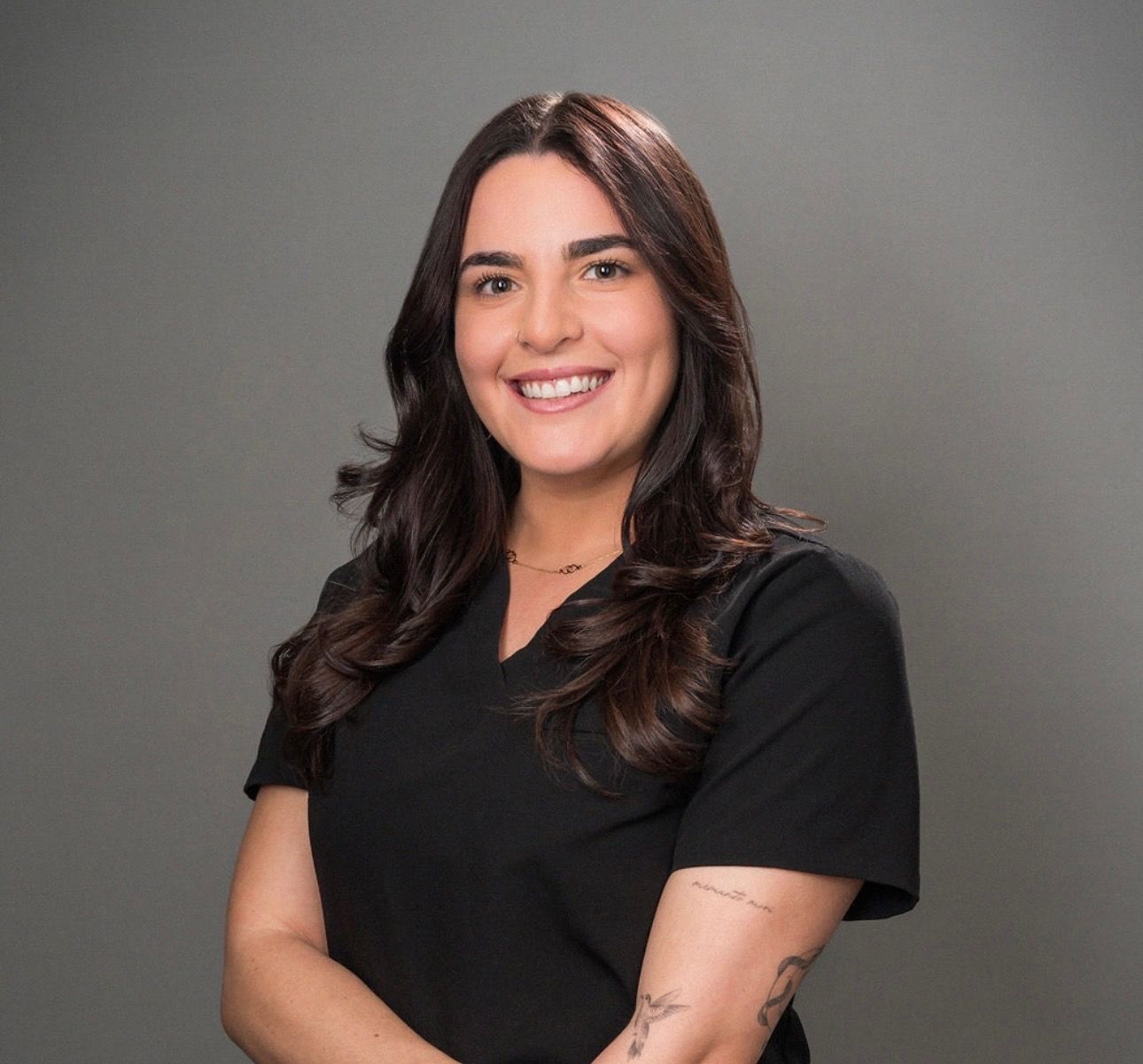 Smiling person with dark hair wearing a black top against a gray background