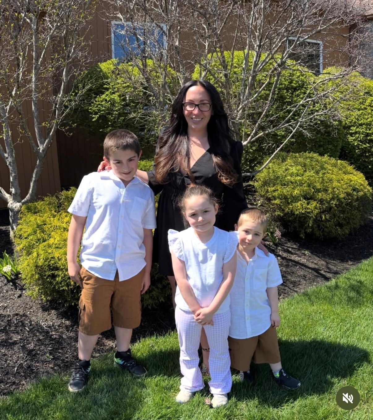 Woman with three children standing on grass in a sunny garden