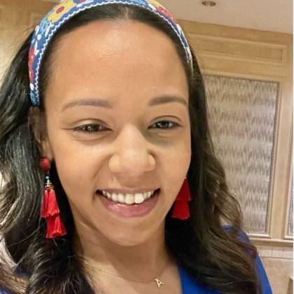 Smiling woman in a colorful headband and red earrings, indoors against a wood-paneled background