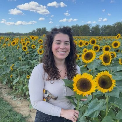Woman smiling in a sunflower field under a blue sky, holding a sunflower