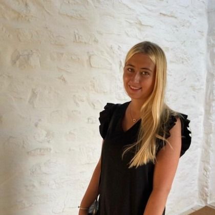 Smiling blonde woman in a black dress standing against a white textured wall