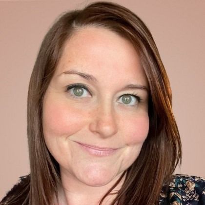 Smiling person with brown hair and green eyes against a soft pink background