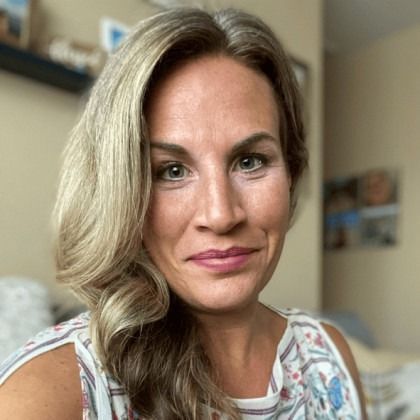 Close-up portrait of a smiling woman with wavy blonde hair in a softly lit room