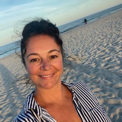 Smiling person taking a selfie on a sandy beach at sunset, wearing a striped shirt.