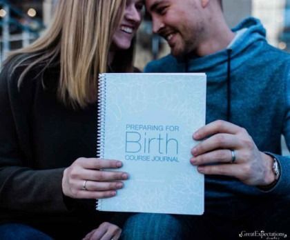 Couple smiling and holding a spiral-bound journal titled “Preparing for Birth”