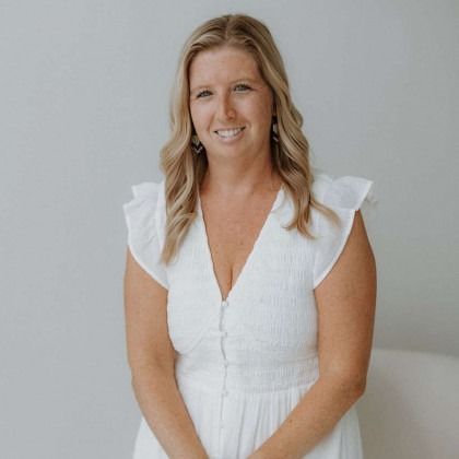 Woman in a white dress smiling against a light gray background
