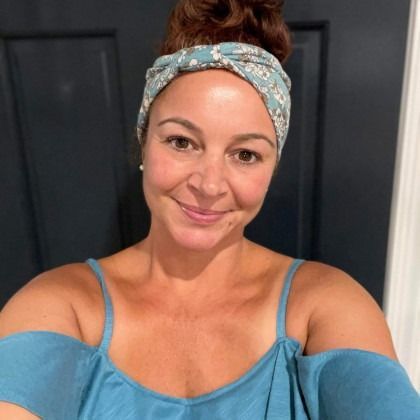 Woman in a blue off-shoulder top smiling indoors, wearing a patterned headband.