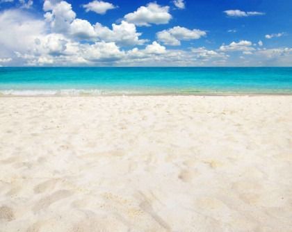 Sunny beach with white sand, turquoise water, and a blue sky with scattered clouds