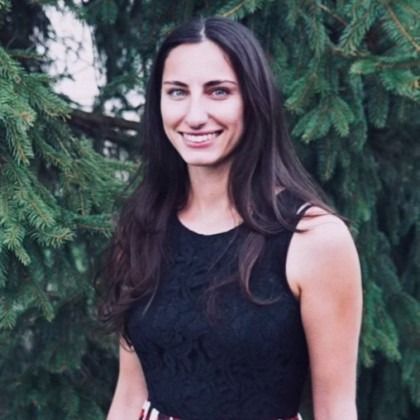 Smiling woman in a black sleeveless top standing outdoors among green trees