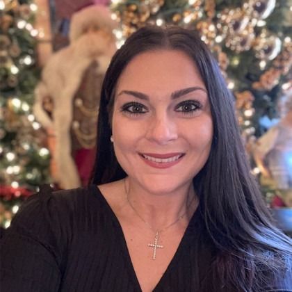 Smiling woman in black top with cross necklace in front of a decorated Christmas tree