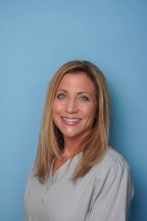Smiling woman in a light gray top against a blue background