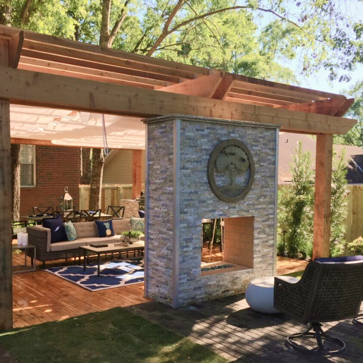 A patio with a stone fireplace and a wooden pergola