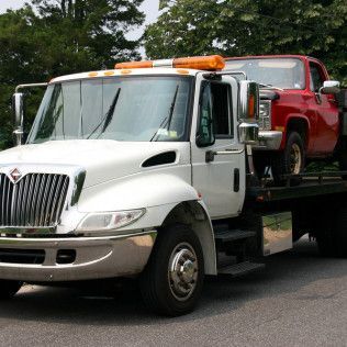 A white tow truck is carrying a red truck on the back of it.
