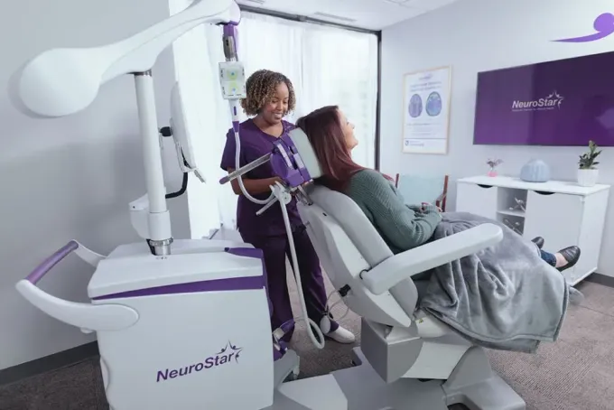 A medical professional adjusting a device for a patient seated in a chair; room setting.