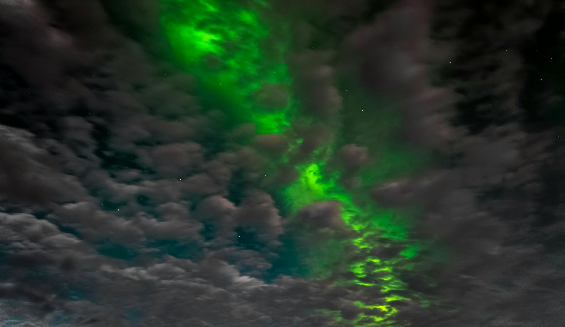 Green aurora borealis glowing through dark, cloudy sky.