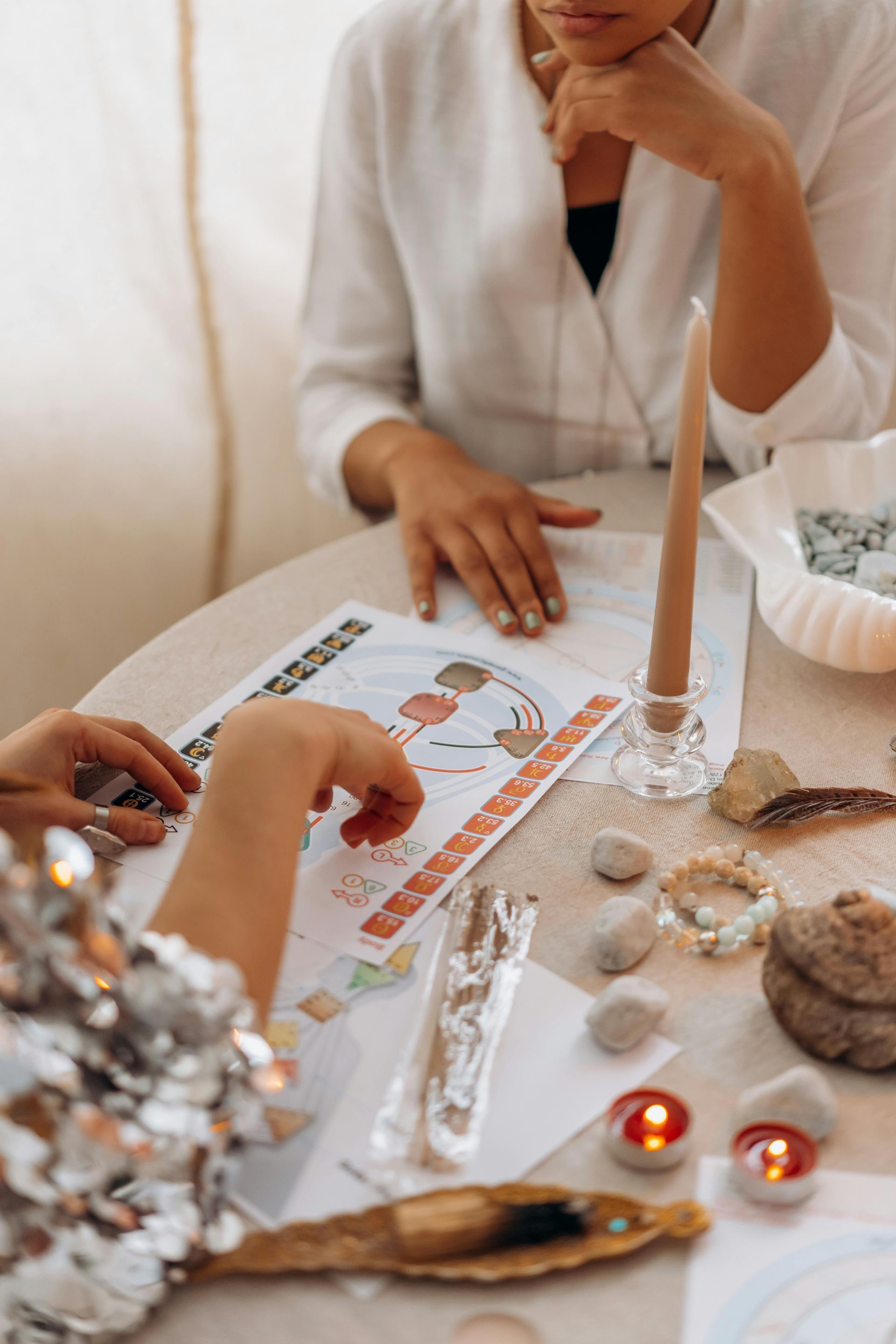 Two people at a table studying a colorful chart with a candle, crystals, and stones.