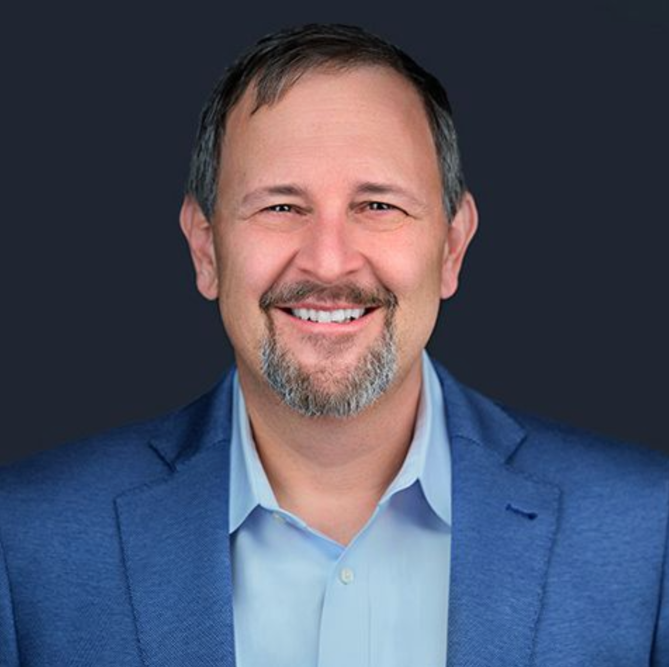 A man with a beard is wearing a blue suit and smiling.