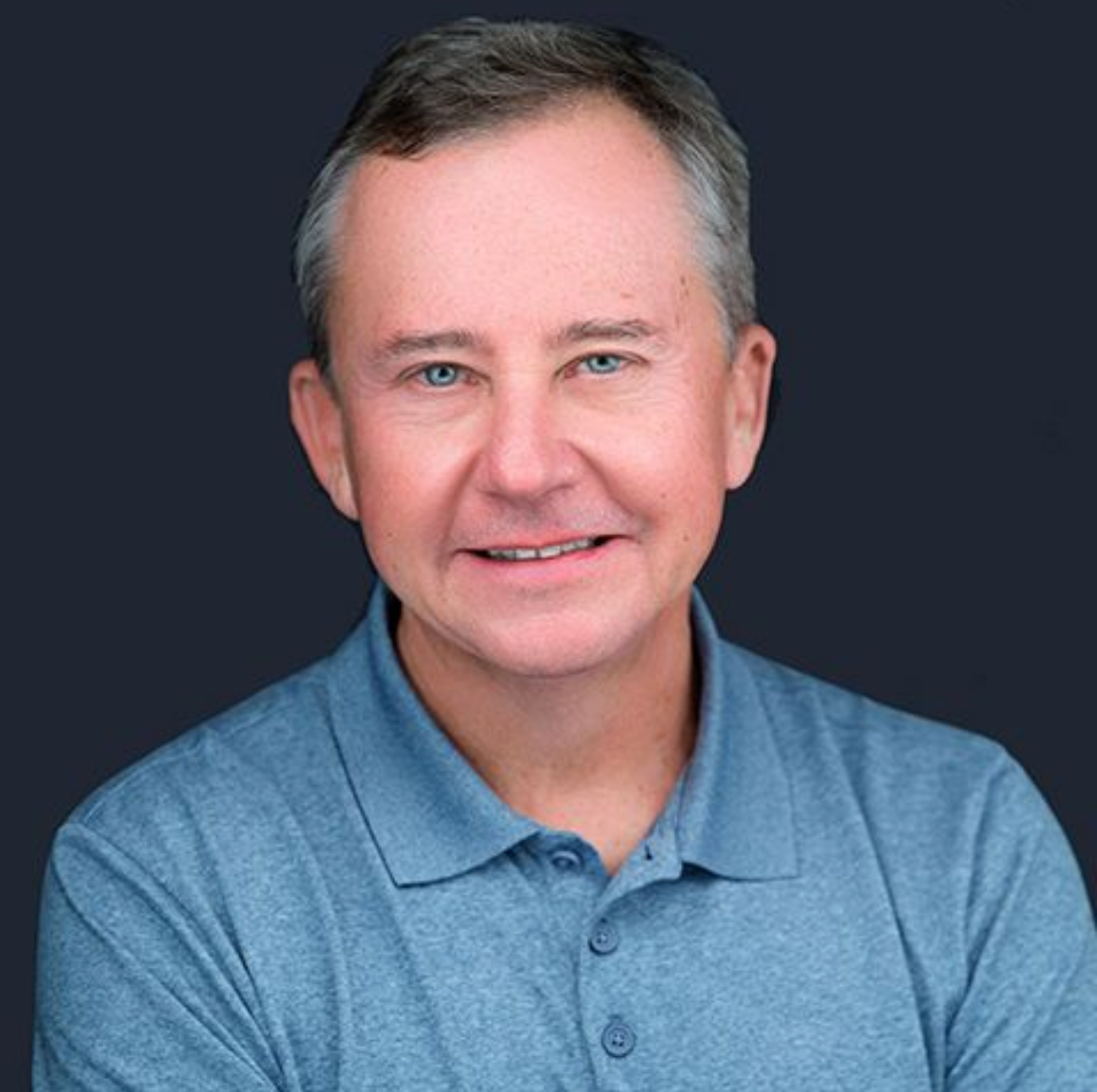 A man in a blue polo shirt is smiling for the camera.