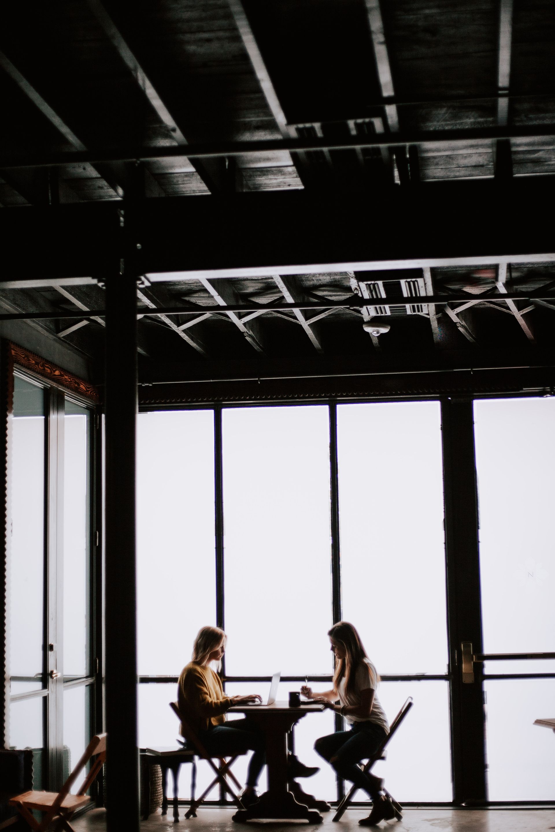 Two people are sitting at a table in front of a window.