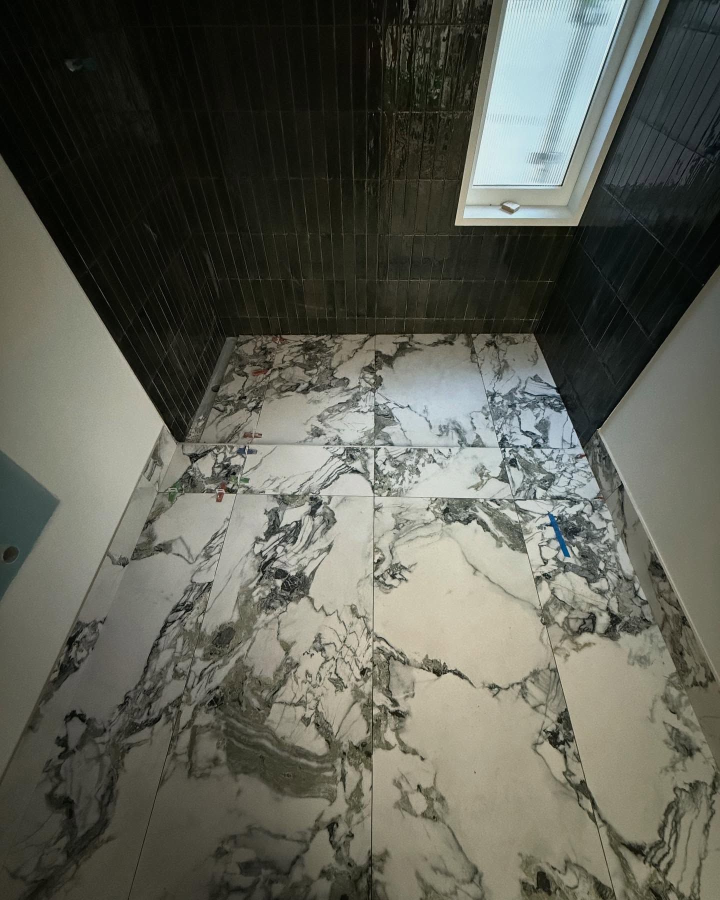 Small tiled bathroom with dark walls, marble-look floor, and a skylight overhead.
