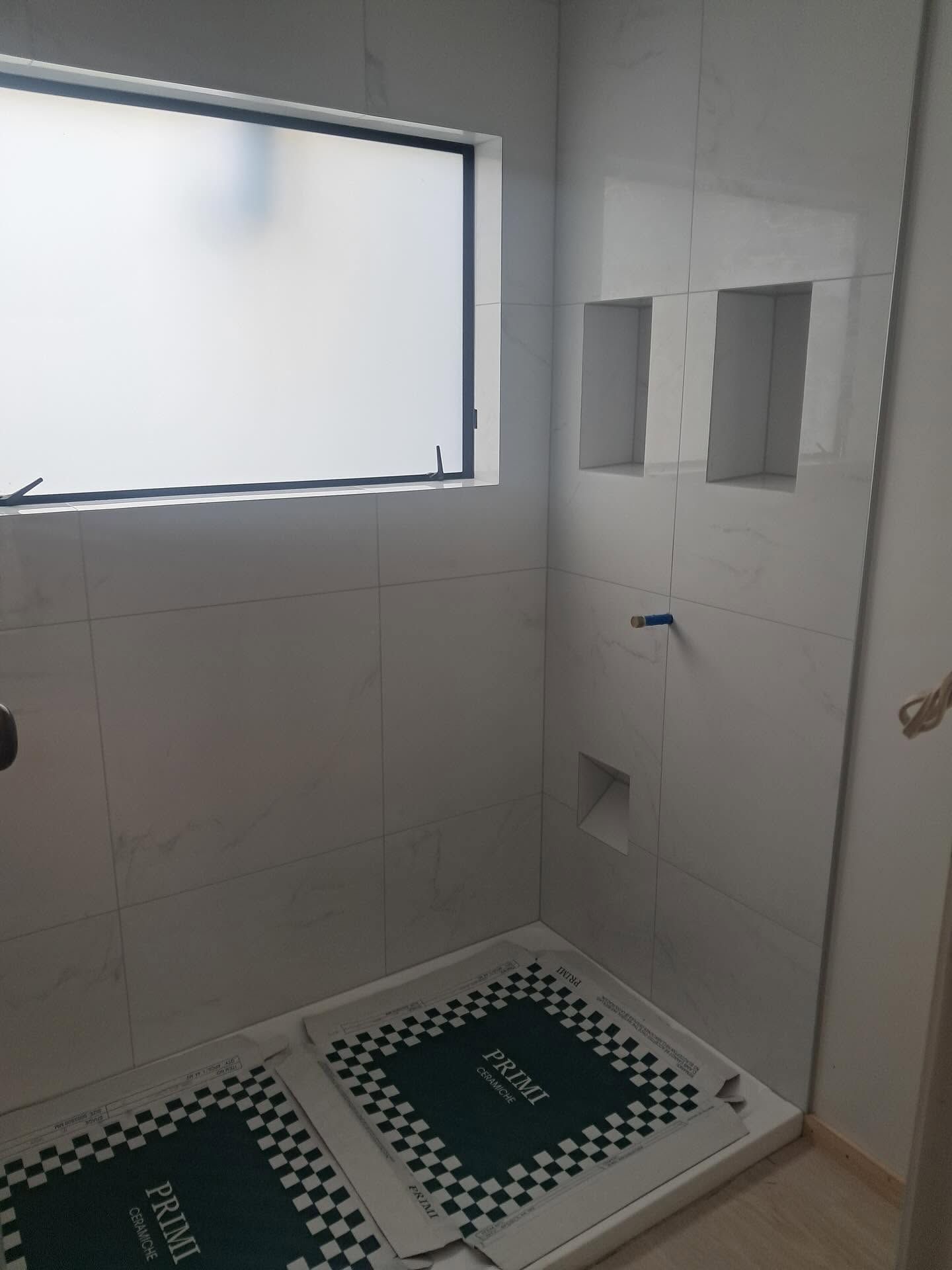 Small tiled bathroom with a shower area, window, and two green patterned bath mats.