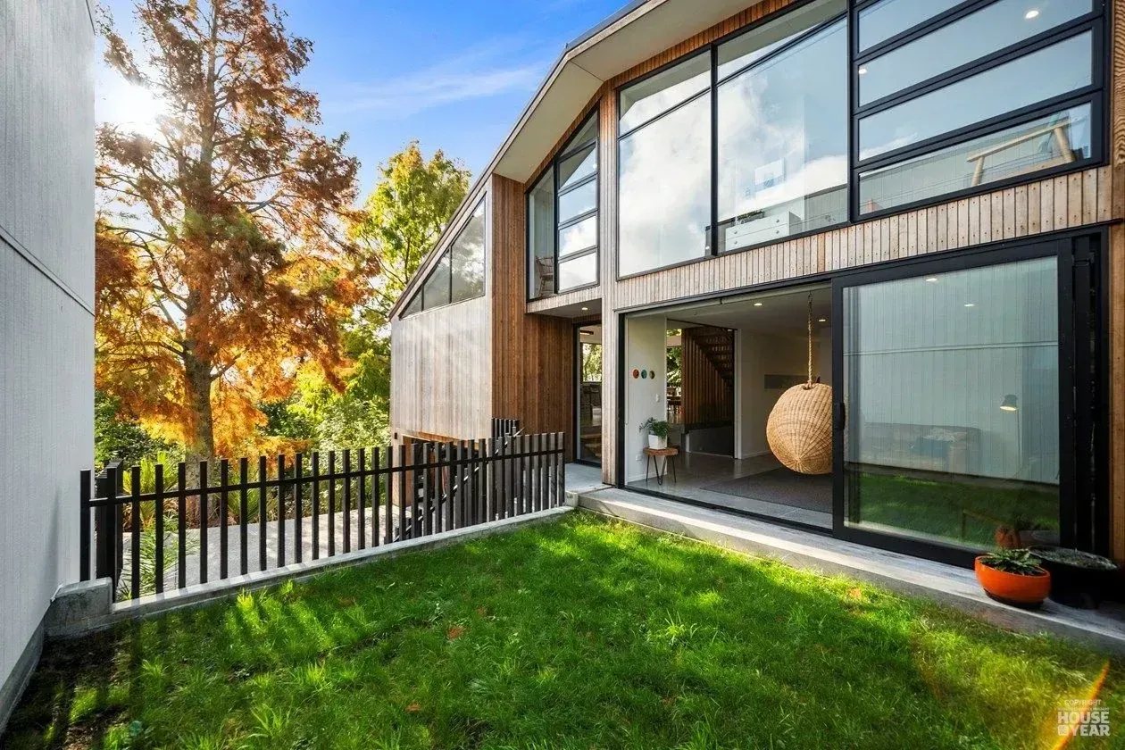 Modern house with large glass windows and a small green backyard patio with black fence and trees