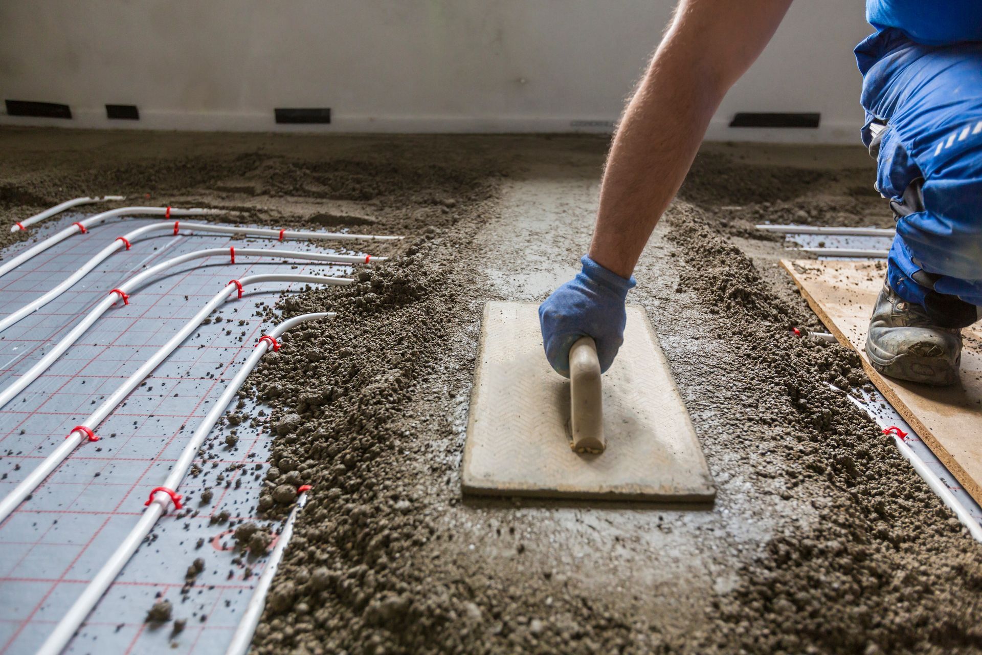 Worker smoothing wet concrete over radiant floor tubing in an indoor construction site