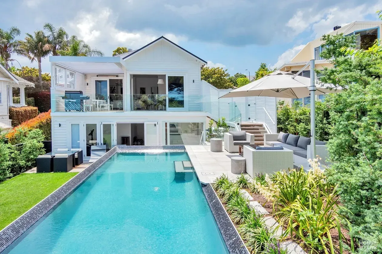 Modern white house with a long turquoise pool and patio seating in a tropical garden