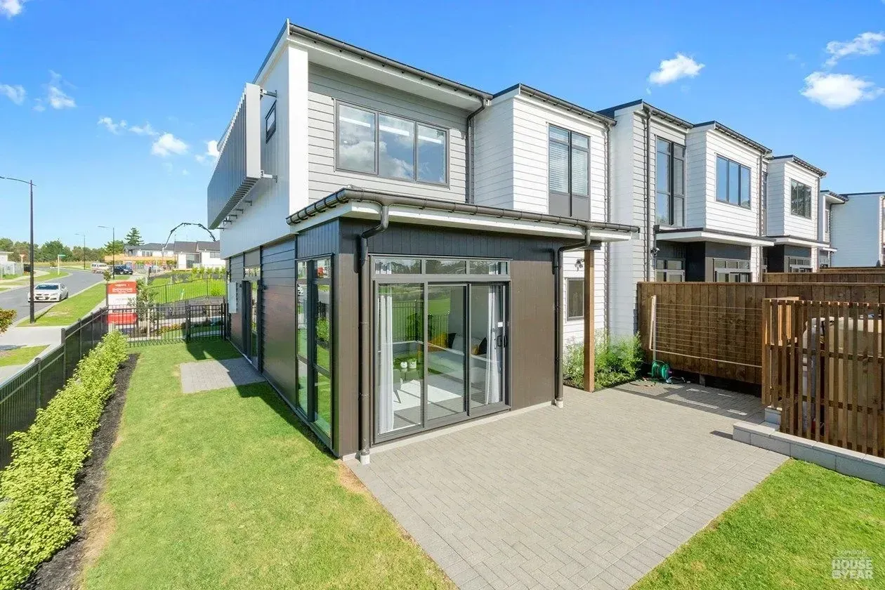 Modern two-story townhouse with glass-front entrance, green lawn, and paved patio in bright daylight