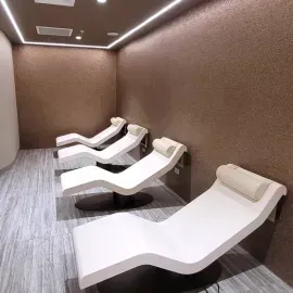 Quiet spa room with four white lounge recliners along a brown wall