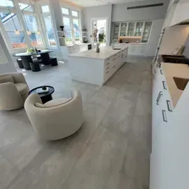 Bright modern kitchen with a large island, white cabinets, and a seating area by sunlit windows.