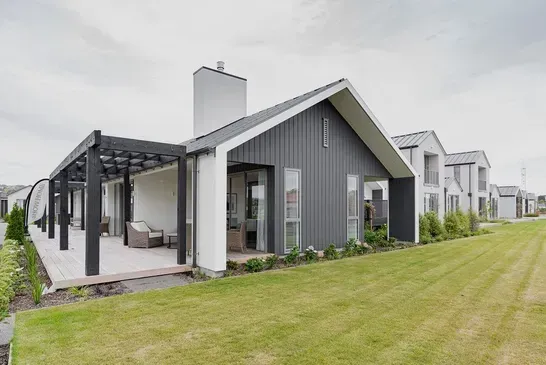 Modern gray house with pergola and porch beside a wide green lawn
