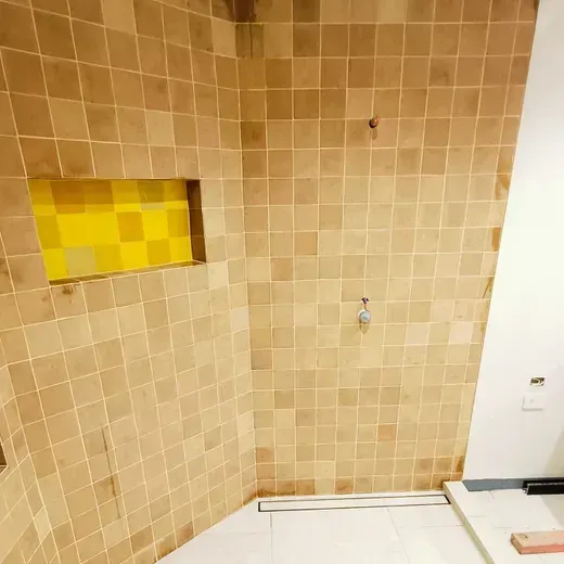 Small tiled bathroom with tan walls, a yellow recessed shelf, and a shower fixture above a white tub.