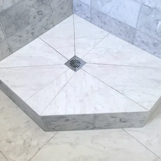 White marble shower floor with a central square drain and surrounding tiled walls