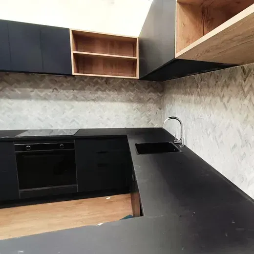 Modern kitchen with black countertops, wood cabinets, and tiled backsplash, viewed from an empty corner