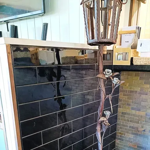 Black tiled outdoor wall with a decorative metal lantern and a climbing vine in front of a glass window.