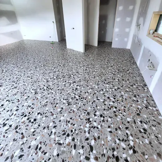 Empty room with terrazzo floor, white walls, and open doorways under renovation