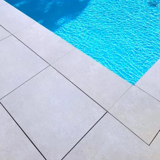 Poolside with light gray tiles beside bright blue water.