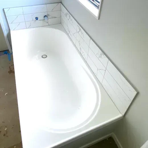 White bathtub with tiled surround beside a window in a bathroom under renovation