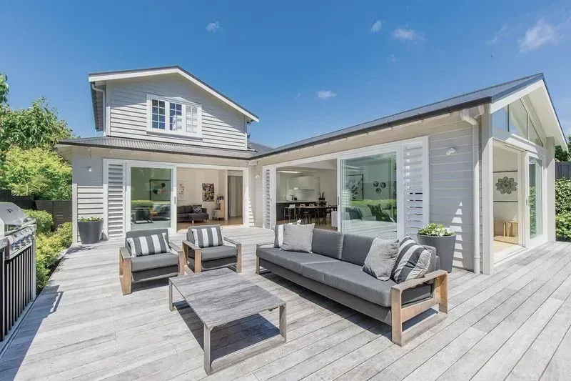 Modern white house patio with gray outdoor seating and a wooden deck under a blue sky