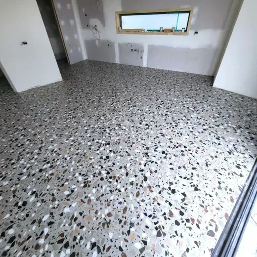 Empty room with speckled terrazzo floor, white walls, and a window on the far wall.