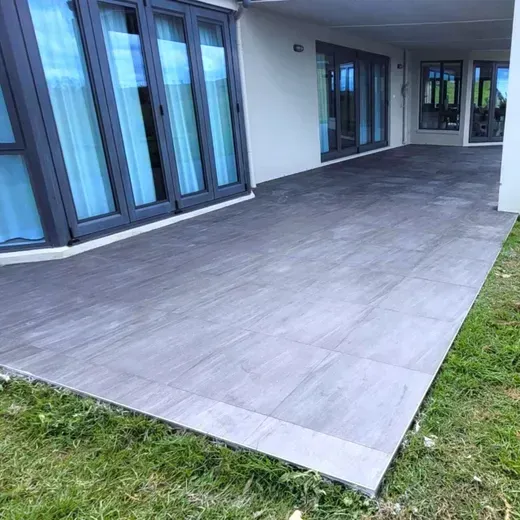 Large gray patio beside blue-framed glass doors and a strip of green grass